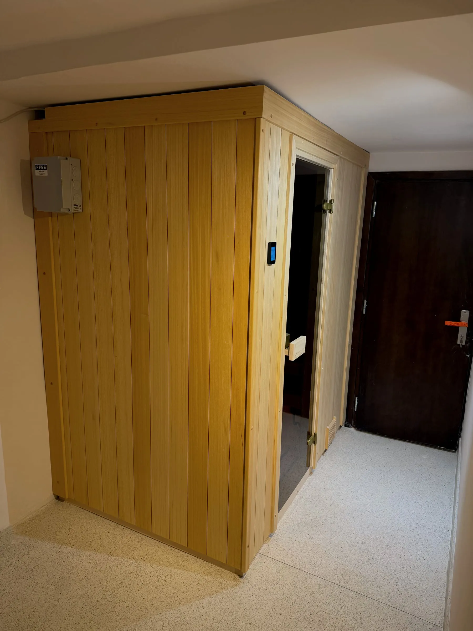 Gotowa kompaktowa sauna ze szklanymi drzwiami i panelem sterowania na ścianie.